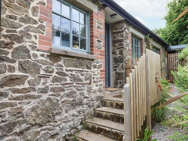Exterior of a stone building with brick accents showing windows door and steps with wooden fence and garden at Hole Farm Stables Bickington near Ashburton