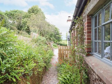 A gravel path with plants and flowers next to a brick and stone house with windows at Hole Farm Stables in Bickington near Ashburton