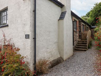 A gravel pathway leading to steps and a wooden gate beside a stone and plaster building with plants on either side at Hole Farm Stables in Bickington near Ashburton
