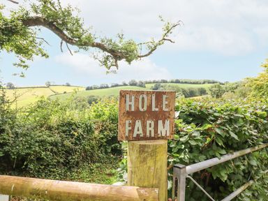 A wooden sign reading Hole Farm on a post near a metal gate with greenery and hills in the background at Hole Farm Stables in Bickington near Ashburton