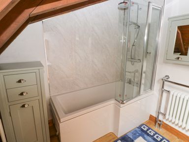A bathroom with a bathtub and glass shower screen a cabinet a radiator and a blue rug at Church Llygad Y Dyffryn in Sarnau near Brynhoffnant