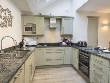 A kitchen with light green cabinets black granite countertops built-in microwave oven and toaster at Leylands Salcombe