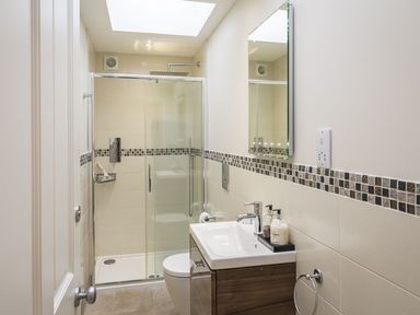 A bathroom with a shower enclosure a sink with soap dispensers and a wall mirror at Leylands in Salcombe
