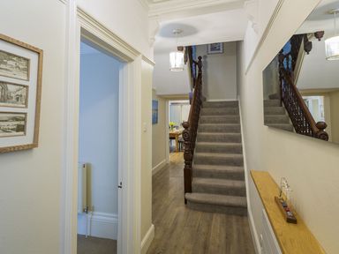 A hallway with a carpeted staircase and wooden banister a mirror on the right wall and framed pictures on the left wall at Leylands in Salcombe