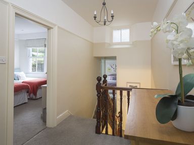 A hallway with carpet and wooden banister with a table and potted plant near two bedrooms with beds visible at Leylands in Salcombe