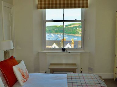 A bedroom with a bed next to a window showing a view of boats and green hills at Leylands in Salcombe