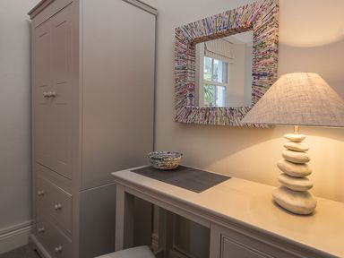 A corner with a wardrobe a table lamp on a table and a mirror on the wall at Leylands in Salcombe