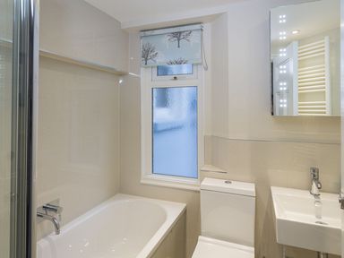 A bathroom with a bathtub a toilet a sink and a window with a roller blind at Leylands in Salcombe