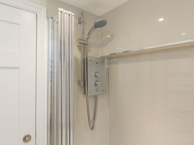 A shower area with a handheld showerhead and control panel in a bathroom at Leylands in Salcombe