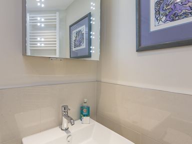 A bathroom sink with a faucet a hand soap dispenser and a framed picture on the wall at Leylands in Salcombe