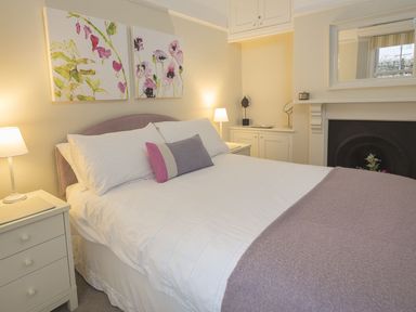 A bedroom with a double bed bedside tables lamps flower paintings and a fireplace at Leylands in Salcombe