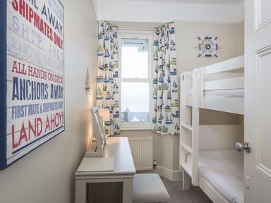 A small bedroom with bunk beds a desk a window with patterned curtains and a nautical themed wall sign at Leylands in Salcombe