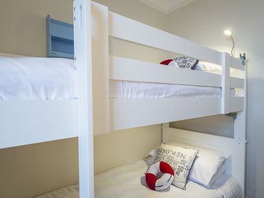 A white bunk bed with pillows and a small red and white circular cushion in a room at Leylands in Salcombe