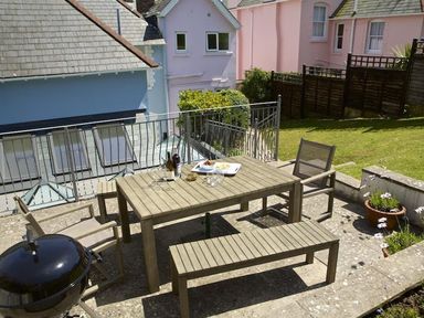 An outdoor patio with a wooden table and chairs a barbecue grill and houses in the background at Leylands Salcombe
