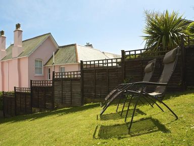 A grassy garden area with two reclining chairs a wooden fence and a light pink house in the background at Leylands in Salcombe