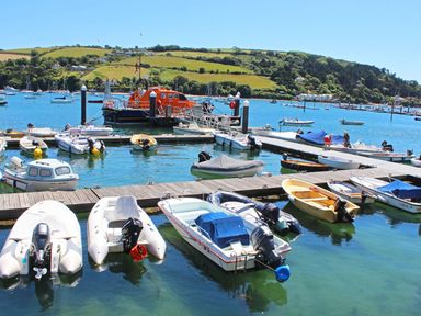 A marina with small boats docked at wooden piers with hills in the background at Leylands Salcombe