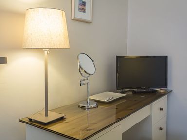 A desk with a lamp a mirror a small TV and a tray in a room