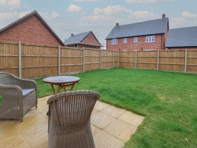 A backyard with grass and a patio area with two wicker chairs and a round wooden table at Inishnee House in Shotley Gate