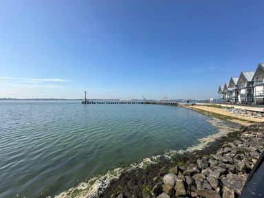 A waterfront with a pier extending into the water and row of buildings with balconies at Inishnee House in Shotley Gate