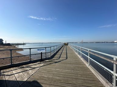 A wooden pier extending over calm water with metal railings under a clear blue sky at Inishnee House in Shotley Gate