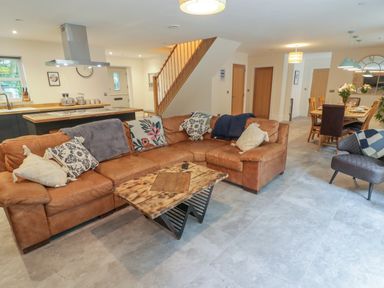 An open plan living room with a brown sectional sofa and wooden coffee table near a kitchen and dining area at The Grove in Wolfsdale near Haverfordwest