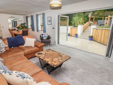 A living room with a leather sofa and wooden coffee table next to an open patio door leading to a tiled outdoor area at The Grove in Wolfsdale near Haverfordwest