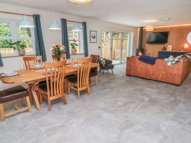 An open plan living and dining area with a wooden dining table and chairs a brown leather sofa a wall mounted television and sliding glass doors at The Grove in Wolfsdale near Haverfordwest