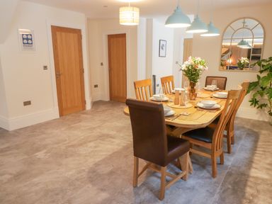 A dining room with a wooden table set with plates and glasses and wooden chairs at The Grove in Wolfsdale near Haverfordwest