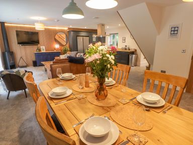 A dining table set with plates bowls glasses and cutlery in an open plan living room with sofas a television and kitchen at The Grove in Wolfsdale near Haverfordwest