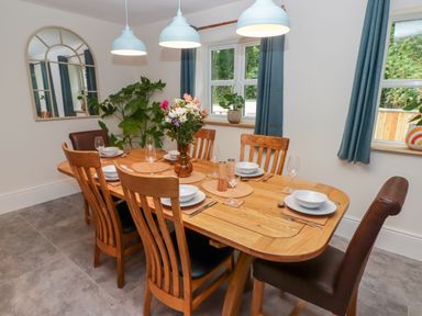 A dining room with a wooden table set for six with plates glasses and flowers at The Grove in Wolfsdale near Haverfordwest