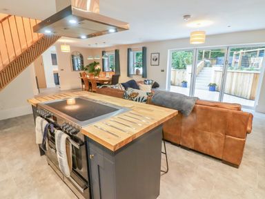 A kitchen with an island and stove next to a living room with sofas and large glass doors at The Grove in Wolfsdale near Haverfordwest