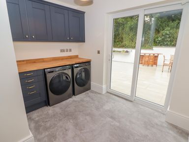 A laundry room with a washing machine and dryer under a wooden countertop and blue cabinets with a sliding glass door to a patio at The Grove in Wolfsdale near Haverfordwest