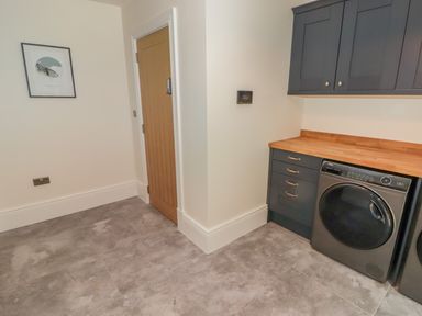 A utility room with a washing machine an oven a wooden door and a framed picture on the wall at The Grove in Wolfsdale near Haverfordwest