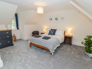 A bedroom with a bed linens and towels bedside tables a dresser a chair and a plant at The Grove in Wolfsdale near Haverfordwest