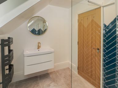A bathroom with a wall-mounted sink with brass faucet round mirror wooden door and blue tiled shower at The Grove in Wolfsdale near Haverfordwest