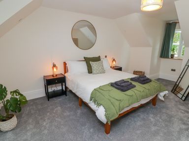 A bedroom with a bed pillows bedside tables lamps a mirror window with curtains a plant and carpeted floor at The Grove in Wolfsdale near Haverfordwest