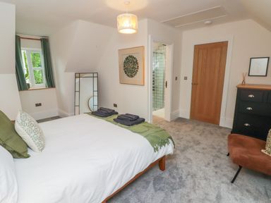 A bedroom with a bed folded towels a standing mirror a door to a bathroom a chest of drawers and a chair at The Grove in Wolfsdale near Haverfordwest