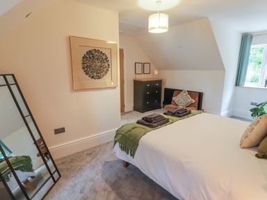 A bedroom with a bed with towels and cushions a mirror a chest of drawers and a window at The Grove in Wolfsdale near Haverfordwest