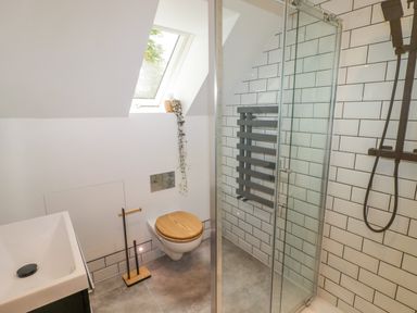 A bathroom with a shower, wall-mounted toilet with wooden seat, sink, window, and black towel radiator at The Grove in Wolfsdale near Haverfordwest