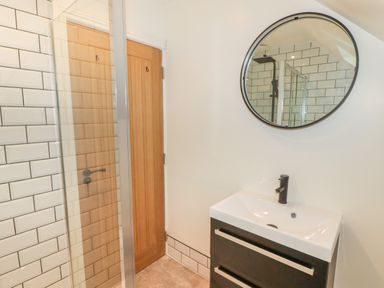A bathroom with a black vanity unit sink a round mirror a wooden door and a tiled shower at The Grove in Wolfsdale near Haverfordwest