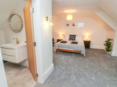 A bedroom with a double bed and bedside tables with lamps next to a bathroom with a sink and round mirror at The Grove in Wolfsdale near Haverfordwest