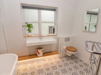 A bathroom with a patterned tile floor a wall-mounted toilet with a wooden seat a floating sink a potted plant and a window at The Grove in Wolfsdale near Haverfordwest