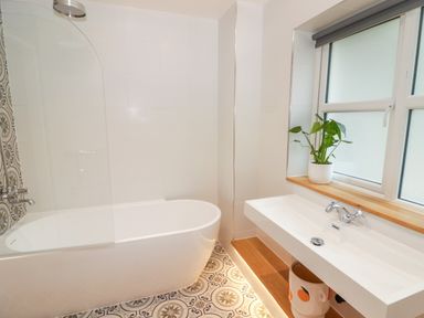 A bathroom with a bathtub shower combination a sink with a faucet a potted plant on the window sill and patterned floor tiles at The Grove in Wolfsdale near Haverfordwest