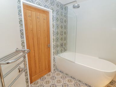 A bathroom with a wooden door a freestanding bathtub with a shower and patterned tiles at The Grove in Wolfsdale near Haverfordwest