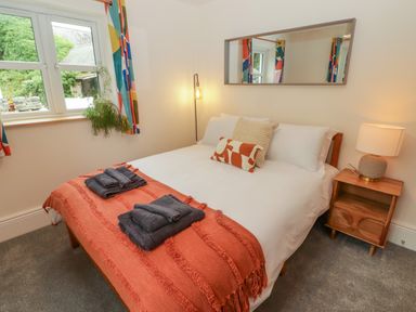 A bedroom with a double bed bedside table lamp and window with colorful curtains at The Grove in Wolfsdale near Haverfordwest