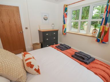 A bedroom with a bed with pillows and folded towels a window with colorful curtains and a chest of drawers at The Grove in Wolfsdale near Haverfordwest