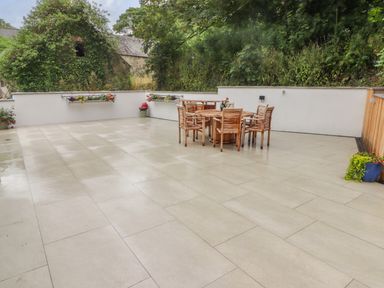 An outdoor patio area with a round wooden table and six wooden chairs surrounded by white walls and plants at The Grove in Wolfsdale near Haverfordwest