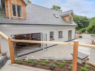An outdoor patio area with wooden railings and small plants below overlooking the open folding doors of a modern house at The Grove in Wolfsdale near Haverfordwest