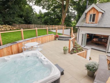 An outdoor patio with a hot tub a round table with chairs potted plants and a house with open doors at The Grove in Wolfsdale near Haverfordwest