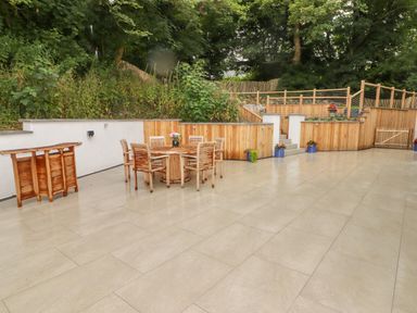 An outdoor patio with a wooden table and chairs surrounded by wooden fencing and greenery at The Grove in Wolfsdale near Haverfordwest